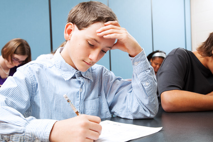 Adolescent middle school boy concentrats on a standardized test in school.