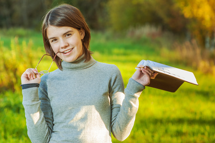 Young girl with book and glasses has reflected against an autumn field.